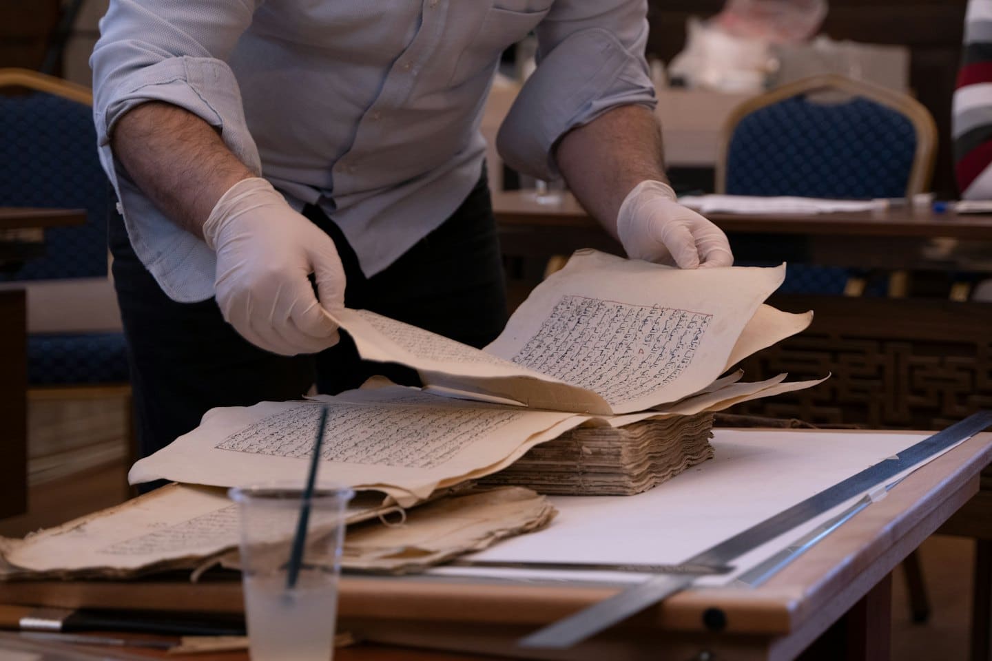 Archivarin mit Handschuhen untersucht alte handschriftliche Dokumente.