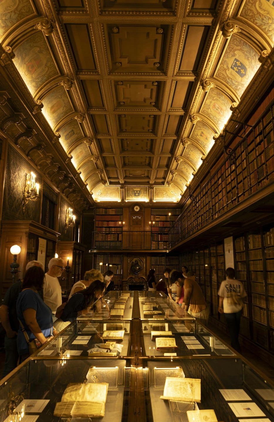 Besucher untersuchen historische Dokumente, die in einem reich verzierten Bibliotheksarchiv ausgestellt sind.